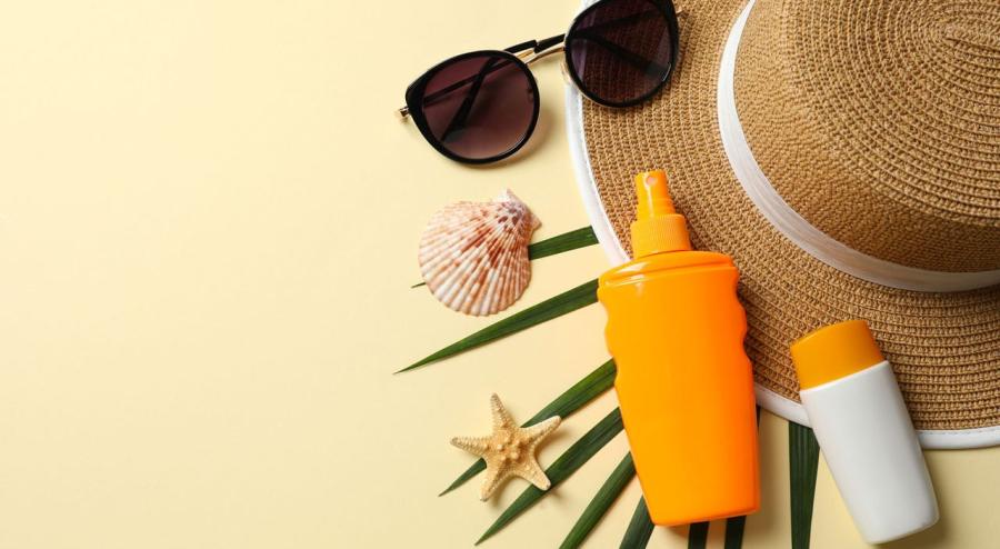 Sun hat, sunglasses and sunscreen arranged on a beach-themed background