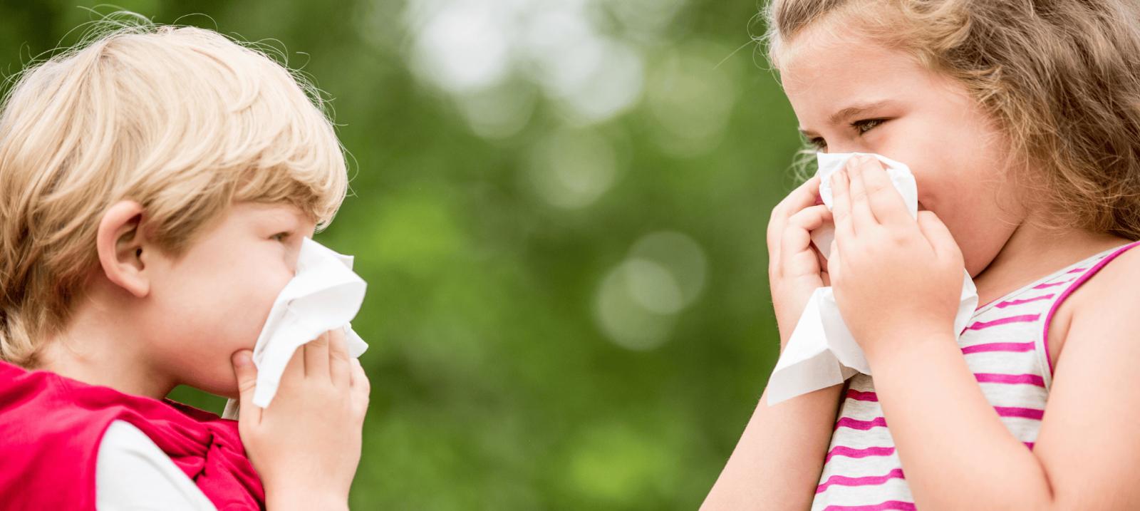 Two young children outdoors holding tissues to their noses with allergy or cold symptoms