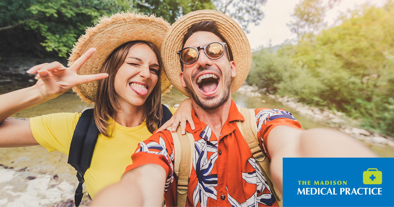 Smiling couple in summer hats taking a cheerful outdoor selfie in a sunny park