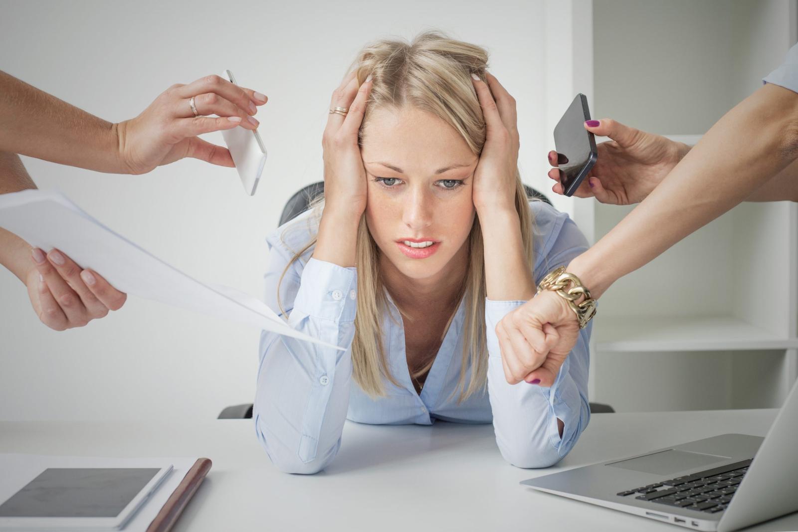 Stressed woman at desk surrounded by urgent tasks and competing demands