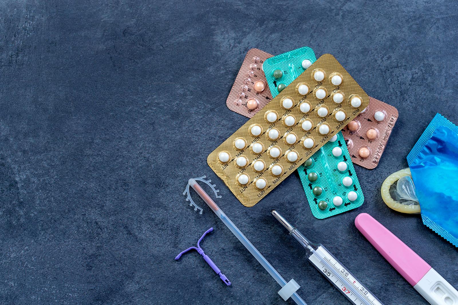 Contraceptive pills, condoms, IUD and syringe arranged on a blue surface