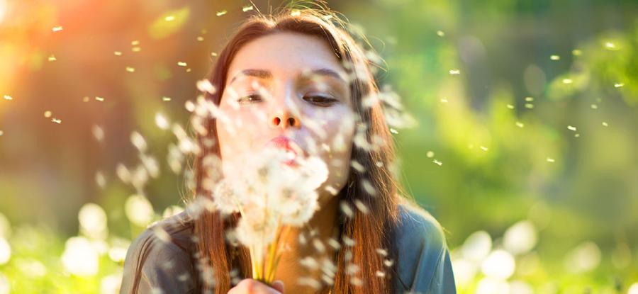 Woman blowing dandelion seeds outdoors in warm sunlight