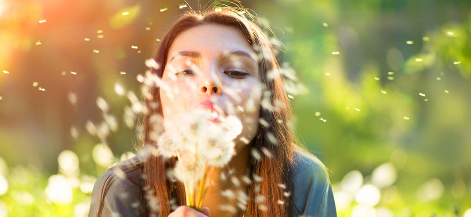 Woman blowing dandelion seeds outdoors in warm sunlight