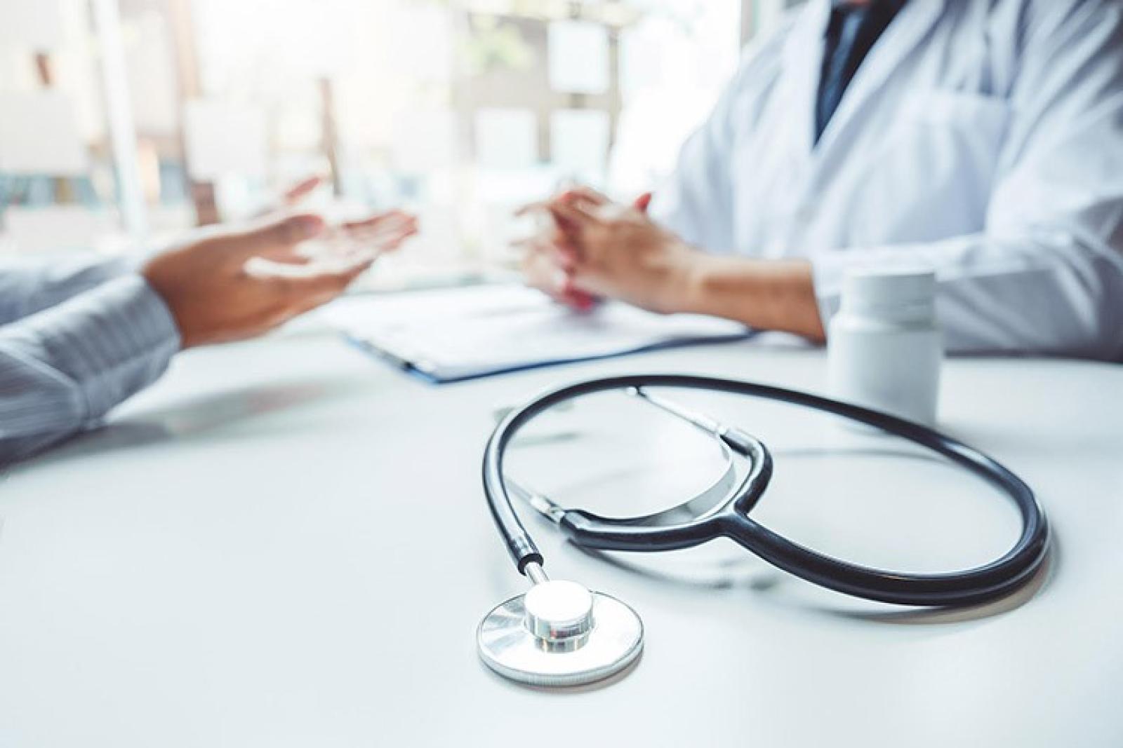 Doctor consulting with a patient across a desk, with a stethoscope in the foreground