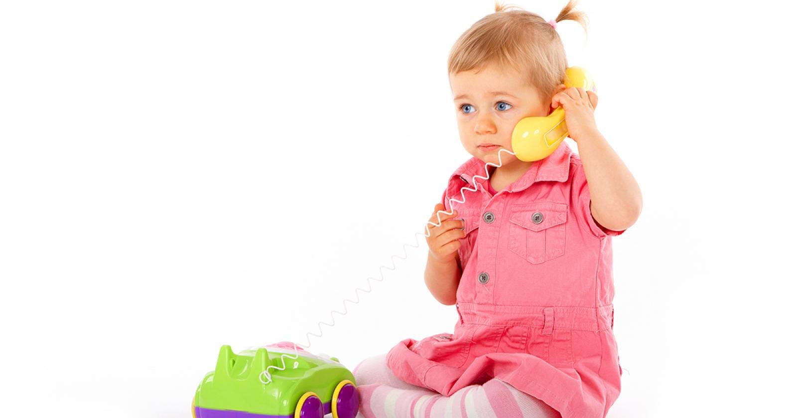 Young child in pink dress holding toy phone, suggesting baby and child health support