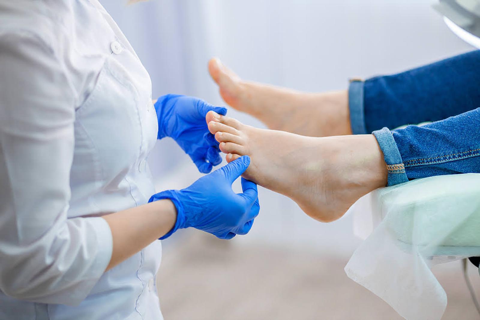 Clinician in blue gloves examining a patient's bare feet during a podiatry-style consultation