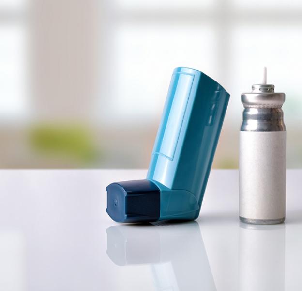 Blue asthma inhaler beside a silver aerosol canister on a white surface