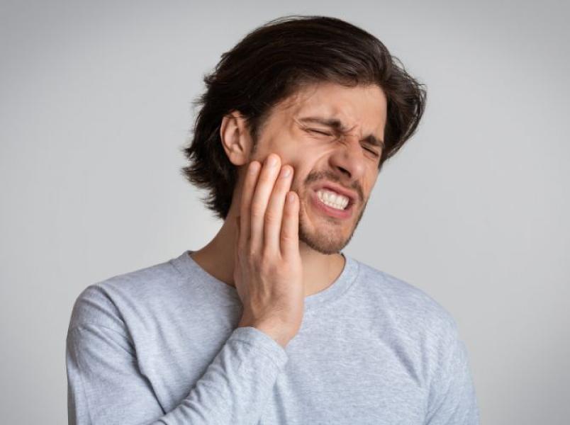 Man holding his jaw in pain, suggesting toothache, jaw pain or facial discomfort