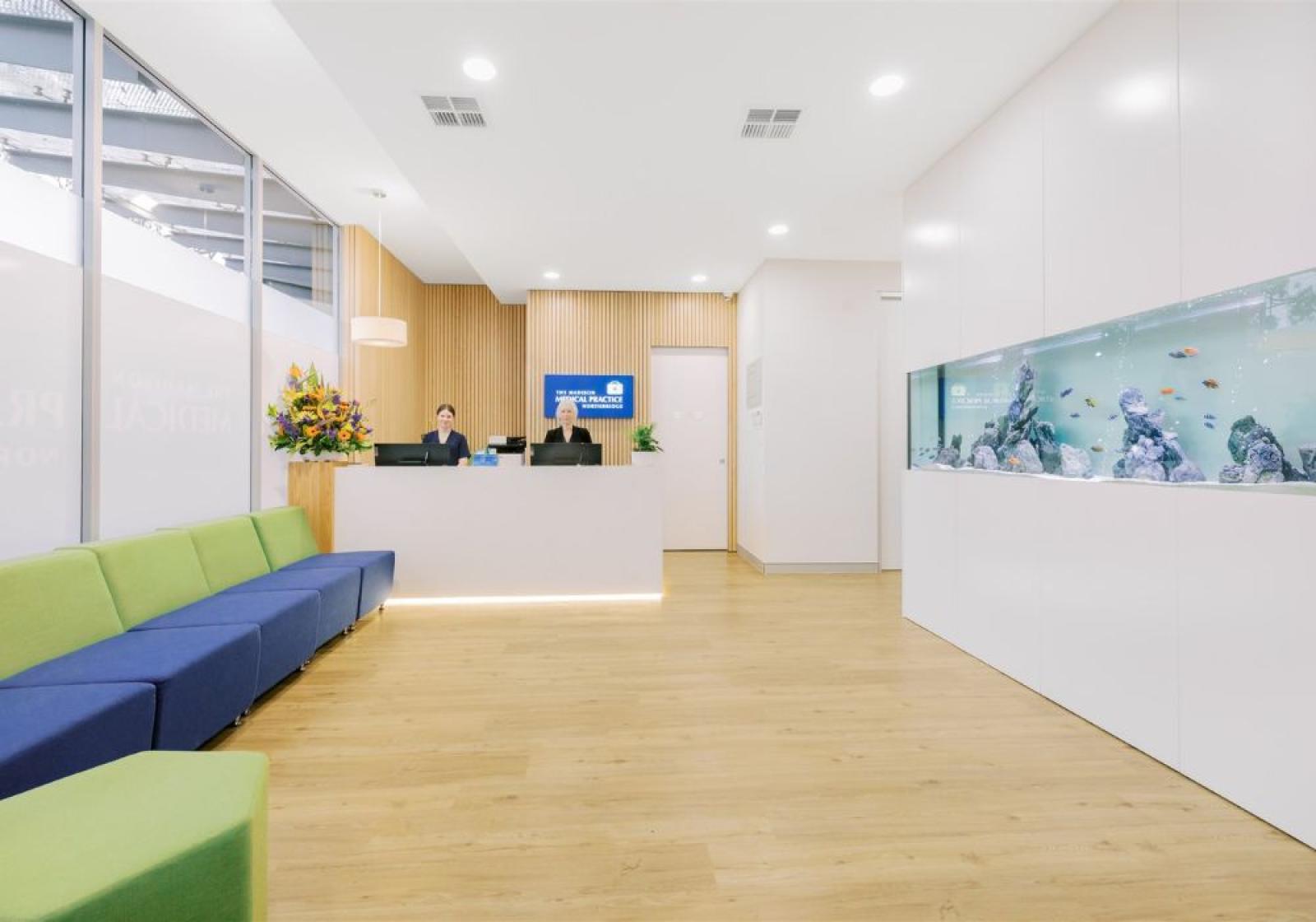 Bright medical practice reception area with bench seating, front desk and a large wall aquarium